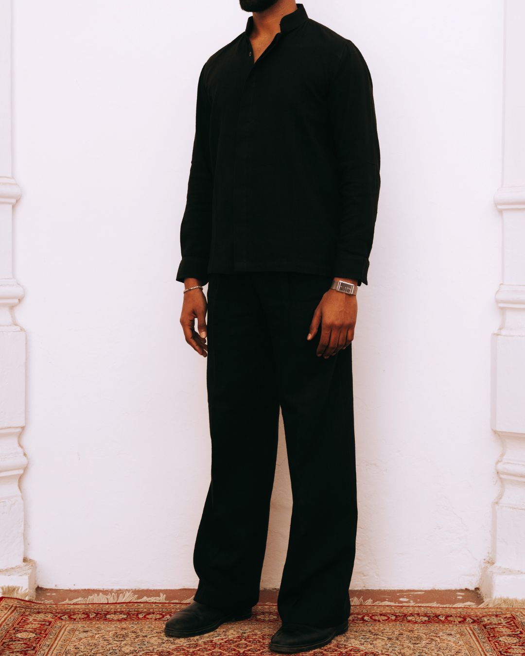 Person wearing a black outfit standing against a white wall. Sarmad Clothing collection by sukhanvar Mens Darwesh Co ord Set Shirt and wide leg pants Trouser Kala Cotton from kutch Bhujodi