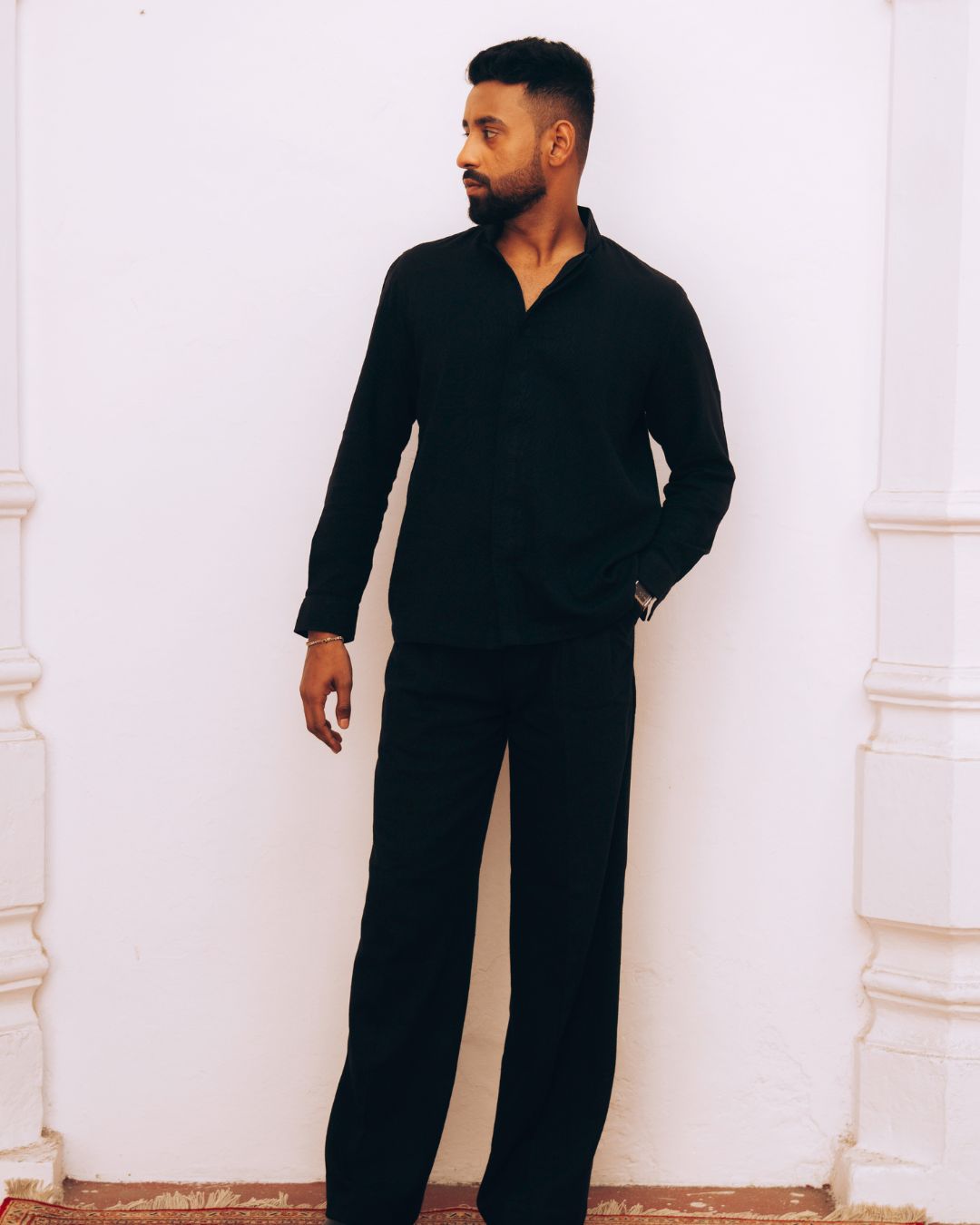 Man wearing a black outfit standing against a white wall. Sarmad Clothing collection by sukhanvar Mens Darwesh Co ord Set Shirt and wide leg pants Trouser Kala Cotton from kutch Bhujodi