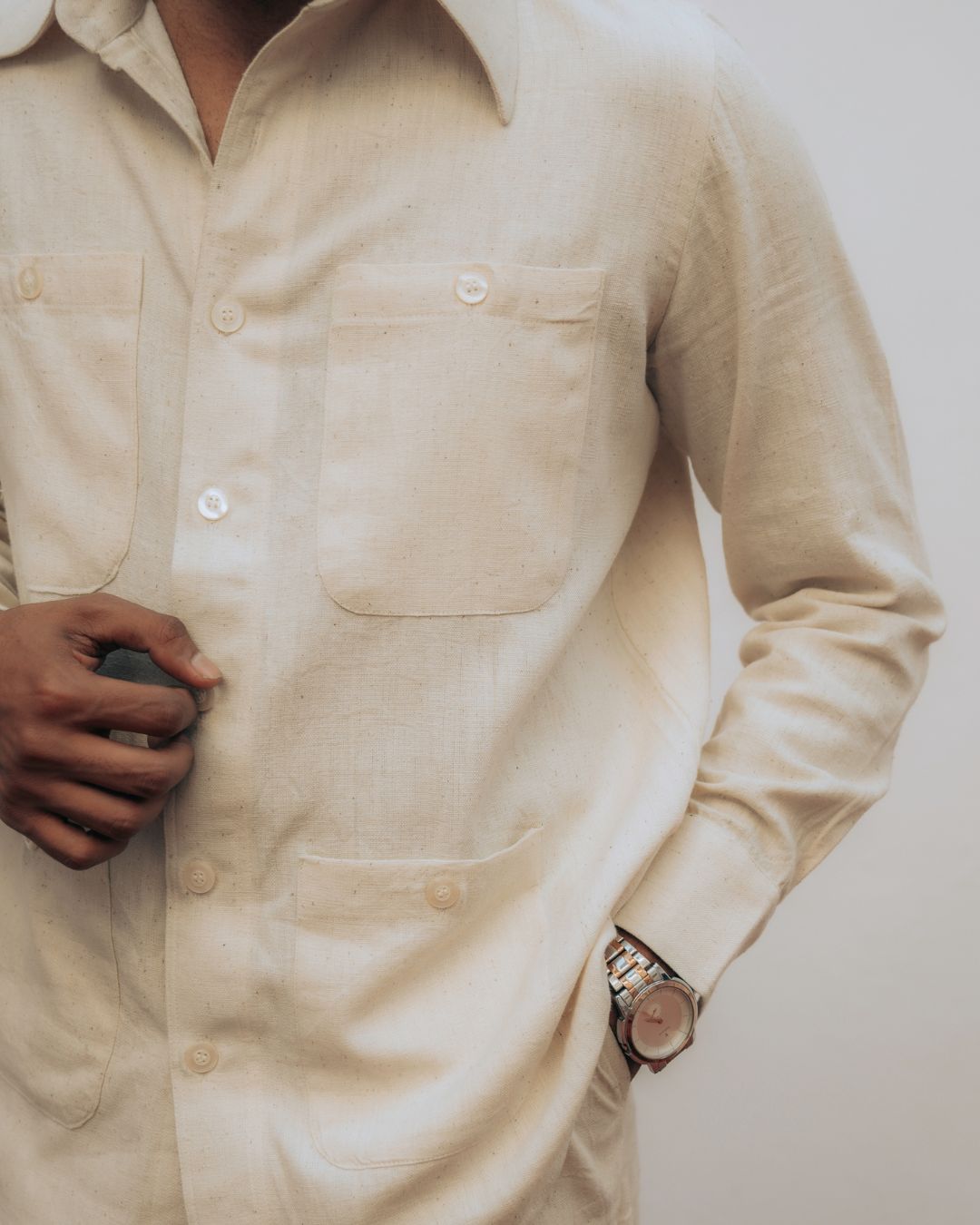 Close-up of a person wearing a beige shirt with a watch on a plain background Sarmad Clothing collection by sukhanvar Mens Raavi Co ord Set 4 Pocket Shirt and Trouser Kala Cotton from kutch Bhujodi