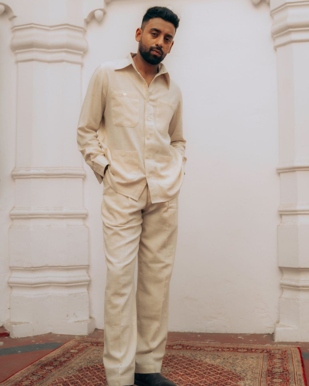Man wearing a beige traditional outfit standing against a white wall. Sarmad Clothing collection by sukhanvar Mens Raavi Co ord Set 4 Pocket Shirt and Trouser Kala Cotton from kutch Bhujodi