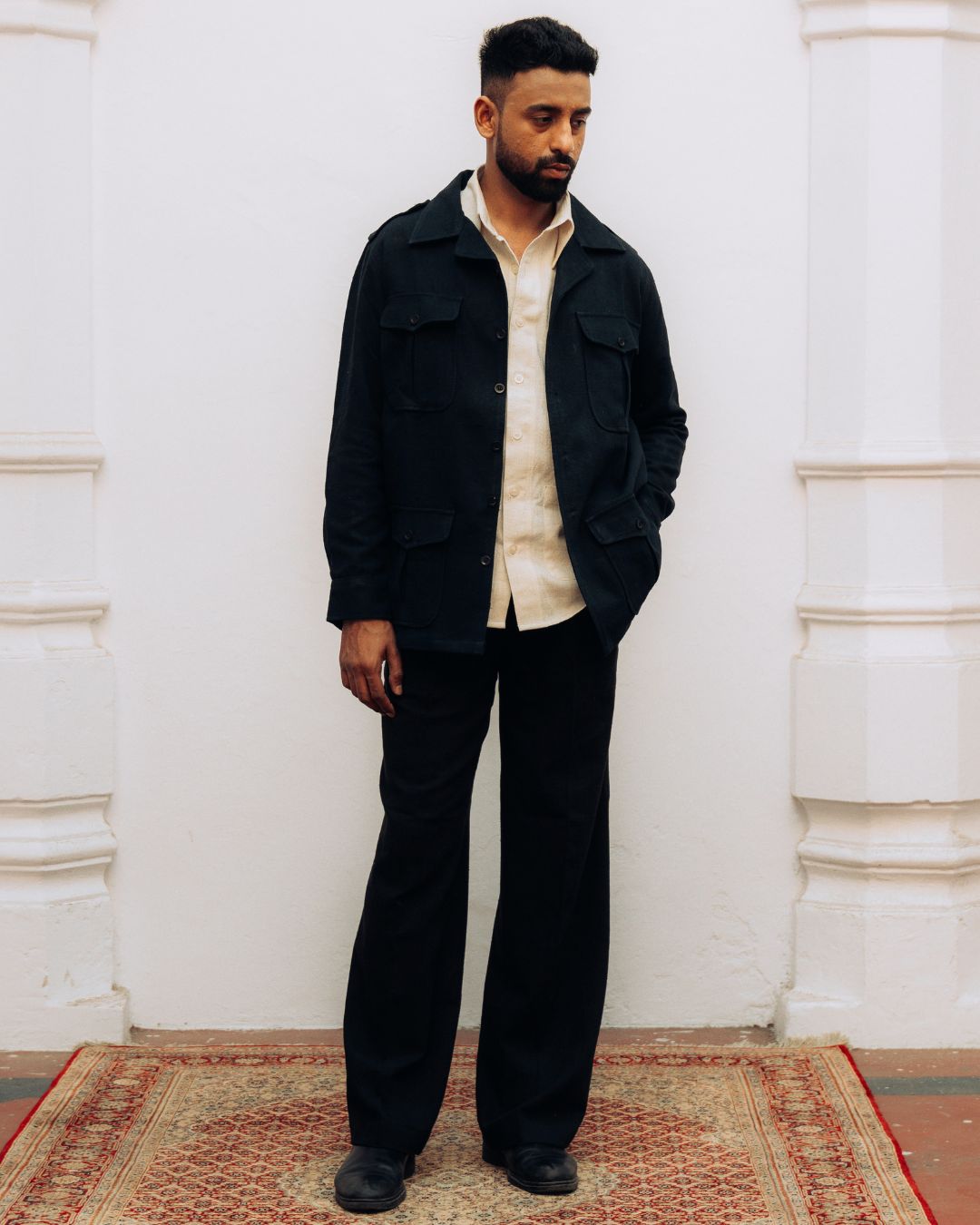 Man wearing a black jacket and pants standing against a white wall. Sarmad Clothing collection by sukhanvar Mens Shacket jacket blazer Raahgir in Kala Cotton from kutch Bhujodi