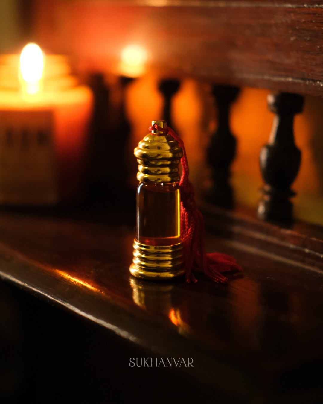 Sukhanvar Hijr Attar smoky oud perfume oil in a glass bottle with gold metal cap and red tassel on a dark wooden shelf.
