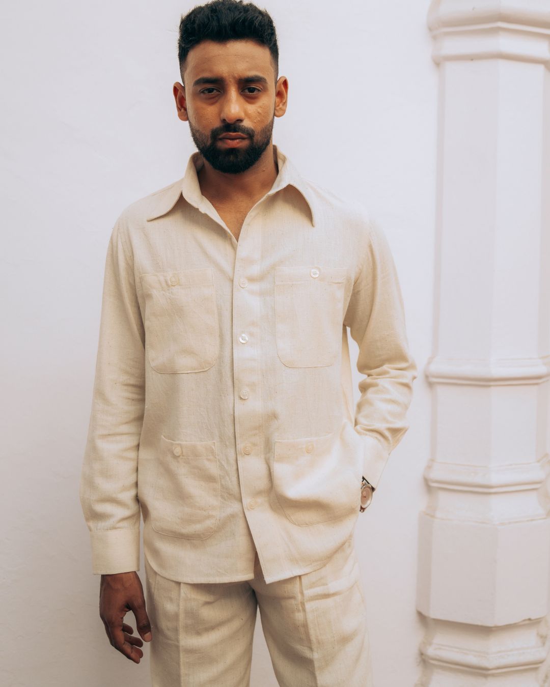 Man wearing a beige shirt and pants against a white wall. Sarmad Clothing collection by sukhanvar Mens Raavi Co ord Set 4 Pocket Shirt and Trouser Kala Cotton from kutch Bhujodi
