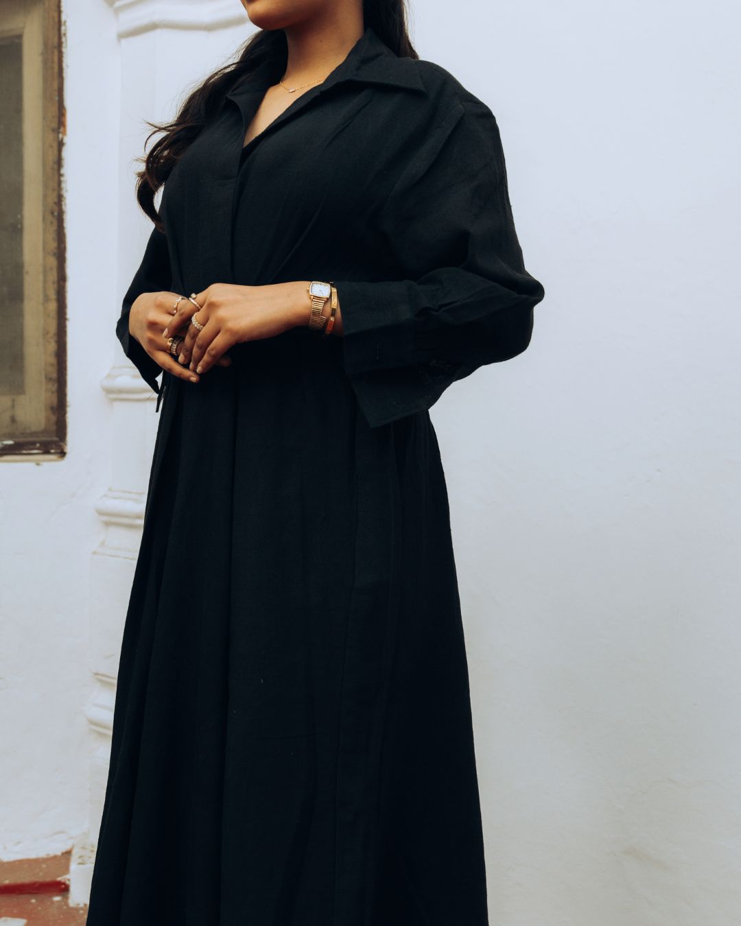 Person wearing a black long-sleeve dress against a white wall. Sarmad Clothing collection by sukhanvar Raqs Flowing Dress in KalaCotton from kutch Bhujodi